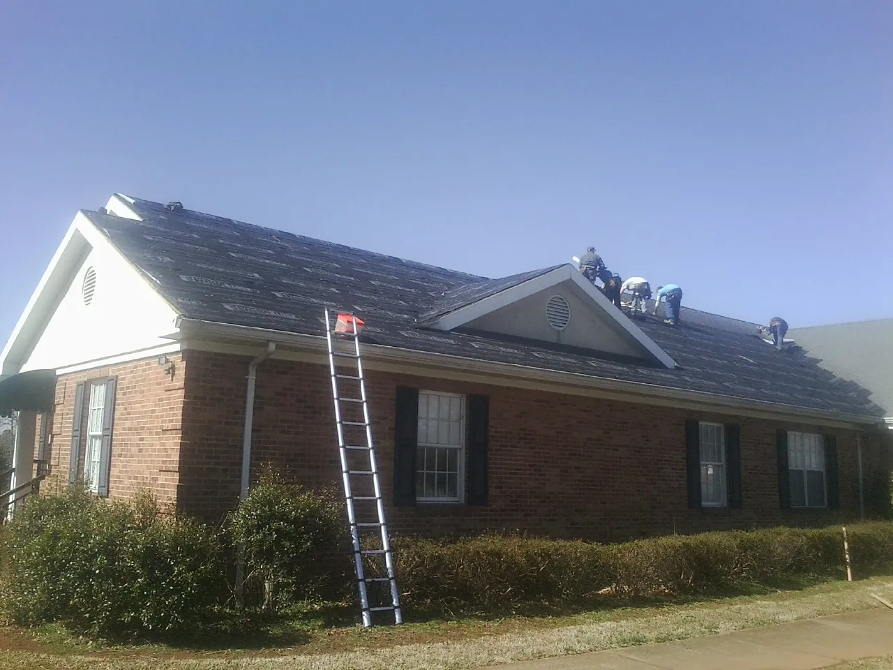 Crew tearing shingles off a brick ranch roof with a ladder set — Metal Roof Repair work by our crew in Arispe