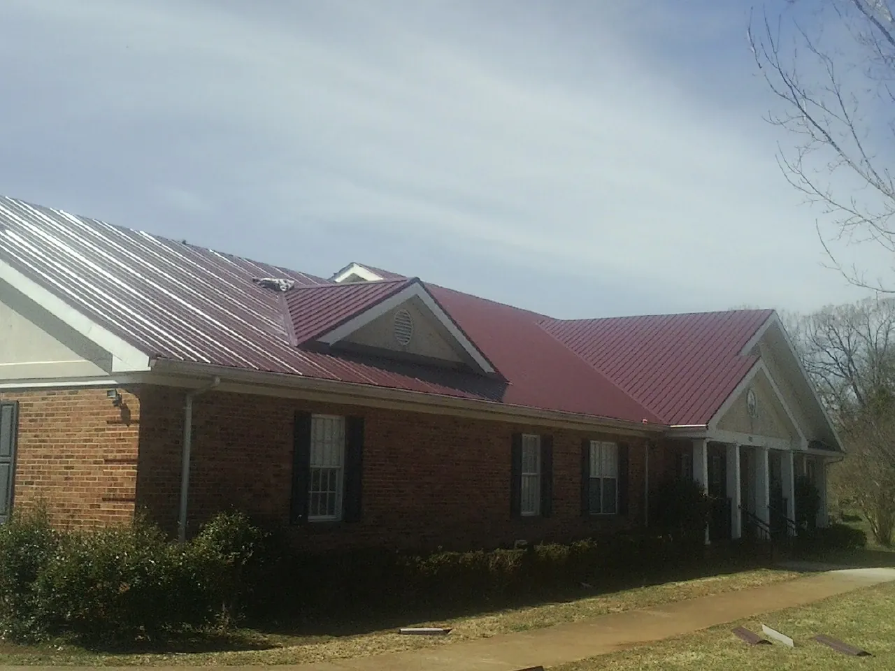 Red metal roof with gabled entries on a long brick building, from a Hail Damage Roof Repair job in Arispe