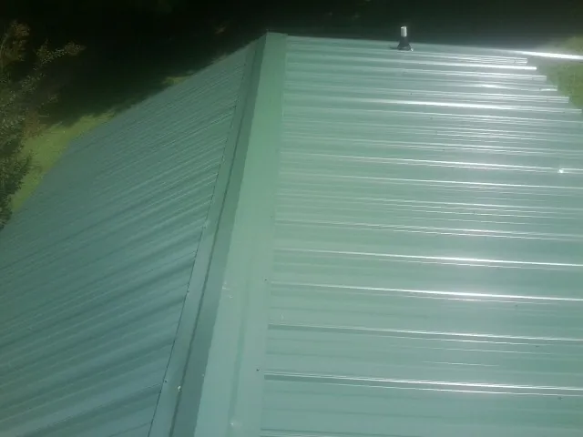 New green metal panels meeting at the ridge of a roof — Flat Roof Repair work by our crew in Arispe