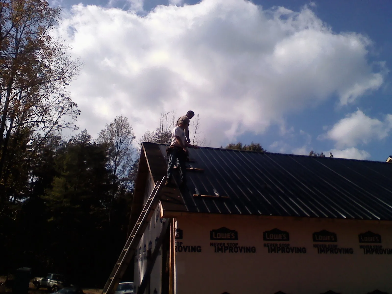 Roofer fastening dark metal panels high against a cloudy sky, from a Roof Inspection job in Arispe