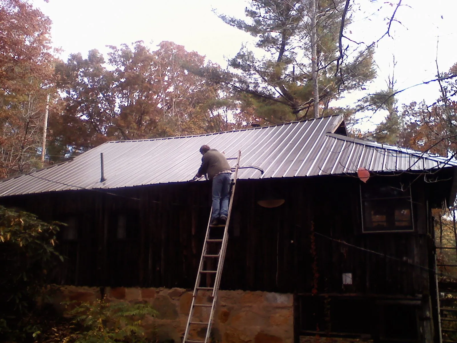 Roofer on a ladder working along the edge of a cabin metal roof in Arispe