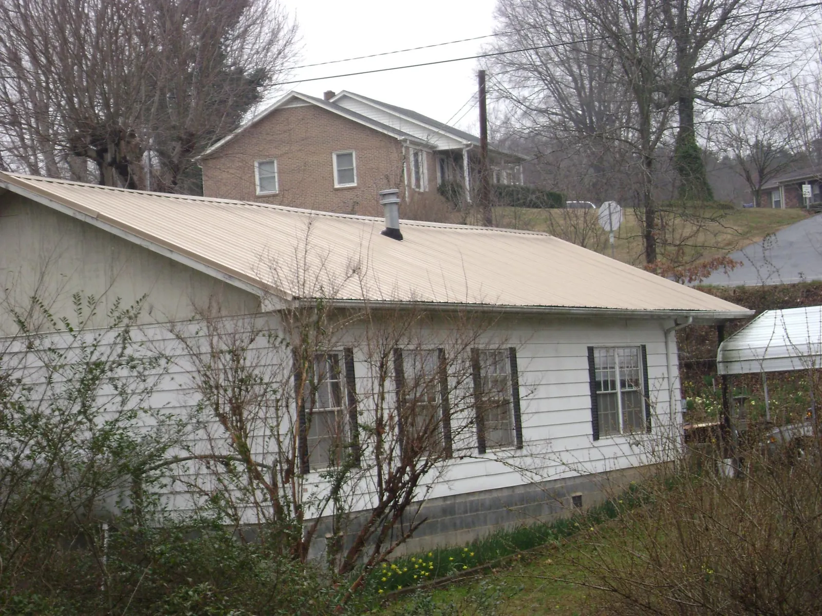 Tan metal roof on a white sided house set into a hillside — Commercial Roofing by Roofing Brothers in Arispe